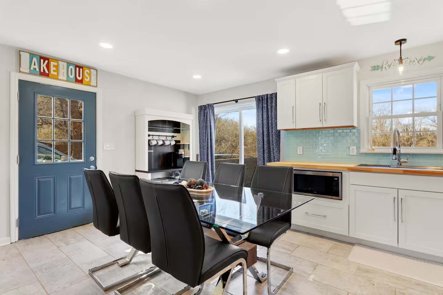 Cozinha moderna com mesa de vidro, cadeiras pretas e porta azul.