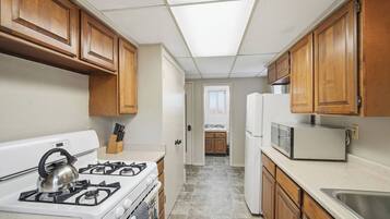 A compact kitchen with wooden cabinets, a gas stove, a microwave, and a refrigerator.