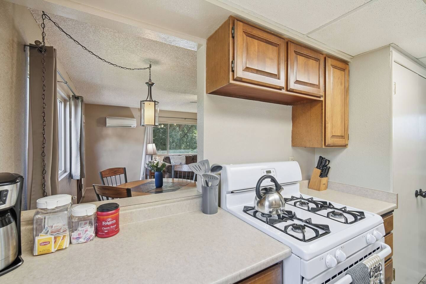 Cocina compacta con estufa a gas, armarios de madera y comedor con mesa y sillas.