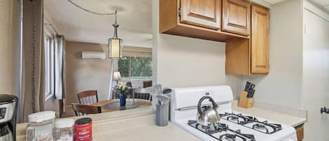 A compact kitchen with a gas stove, wooden cabinets, and a dining area with a table and chairs.