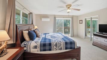 Une chambre à coucher comprenant un lit, un ventilateur de plafond, un téléviseur et une porte-fenêtre coulissante donnant sur un espace extérieur.