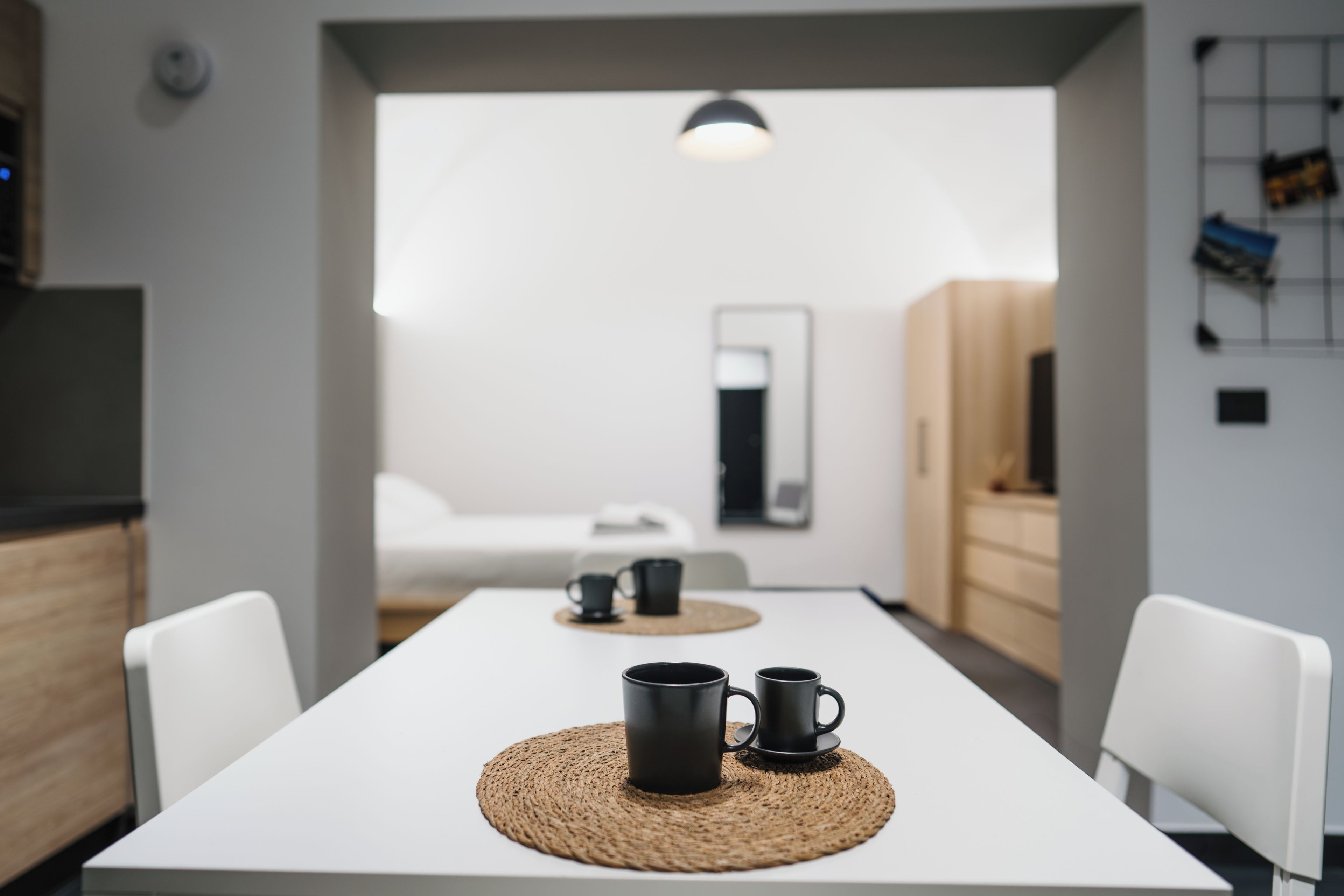 Un espace repas moderne et minimaliste, avec une table blanche, deux tasses noires et un set de table en fibres tressées.