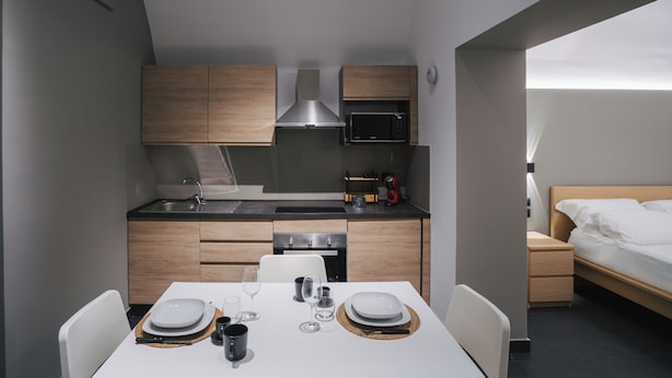 A compact kitchen with modern appliances, a dining area with a table set for two, and a bed in the adjacent room. - Harry's House Trani (Trani)