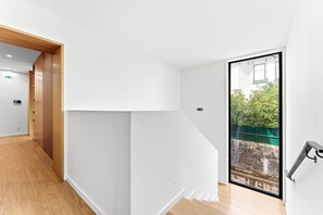 A modern interior with a wooden floor, white walls, and a glass door leading to an outdoor area with greenery. - GuestReady - PoetikBlue - Room 5 (Porto)