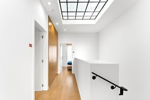 A modern interior with a skylight, wooden flooring, and a white reception desk. - GuestReady - PoetikBlue - Room 5 (Porto)