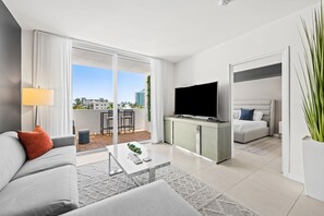 Ein modernes Hotelzimmer mit einer Couch, einem Couchtisch, einem Fernseher und einem Balkon mit Blick auf Gebäude.