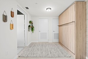 Ein Flur mit einer weißen Tür, einem Holzschrank, einem gemusterten Teppich und an der Wand befestigten Pflanzen.