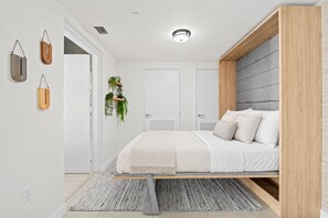 A modern bedroom with a bed, a bedside table, a hanging plant, and a wardrobe. - Luxury Condo Steps from Fort Lauderdale Beach (Fort Lauderdale)