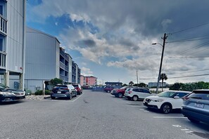 A parking lot with multiple cars, a building with a flat facade, and a clear sky with clouds. - Sandal Suite (Carolina Beach)
