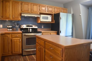 Una cocina con armarios de madera, estufa, horno, microondas y refrigerador.