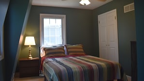 Een slaapkamer met een bed, een nachtkastje, een lamp, een raam en een deur.