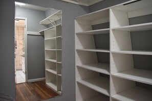 A room with a built-in wardrobe and a mirrored closet door, featuring multiple shelves and a wooden floor. - Spacious Lincoln Home - Sleeps 8 - Perfect for Families & Groups (Lincoln)