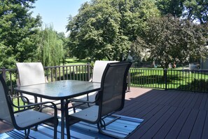 An outdoor patio with a table and chairs, surrounded by a wooden deck and a metal railing. - Spacious Lincoln Home - Sleeps 8 - Perfect for Families & Groups (Lincoln)