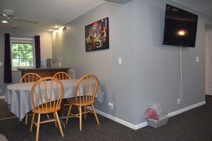 Un comedor con una mesa y sillas, un televisor montado en la pared y una ventana con cortinas.