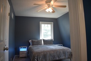 A bedroom with a bed, a nightstand, a ceiling fan, and a window. - Spacious Lincoln Home - Sleeps 8 - Perfect for Families & Groups (Lincoln)