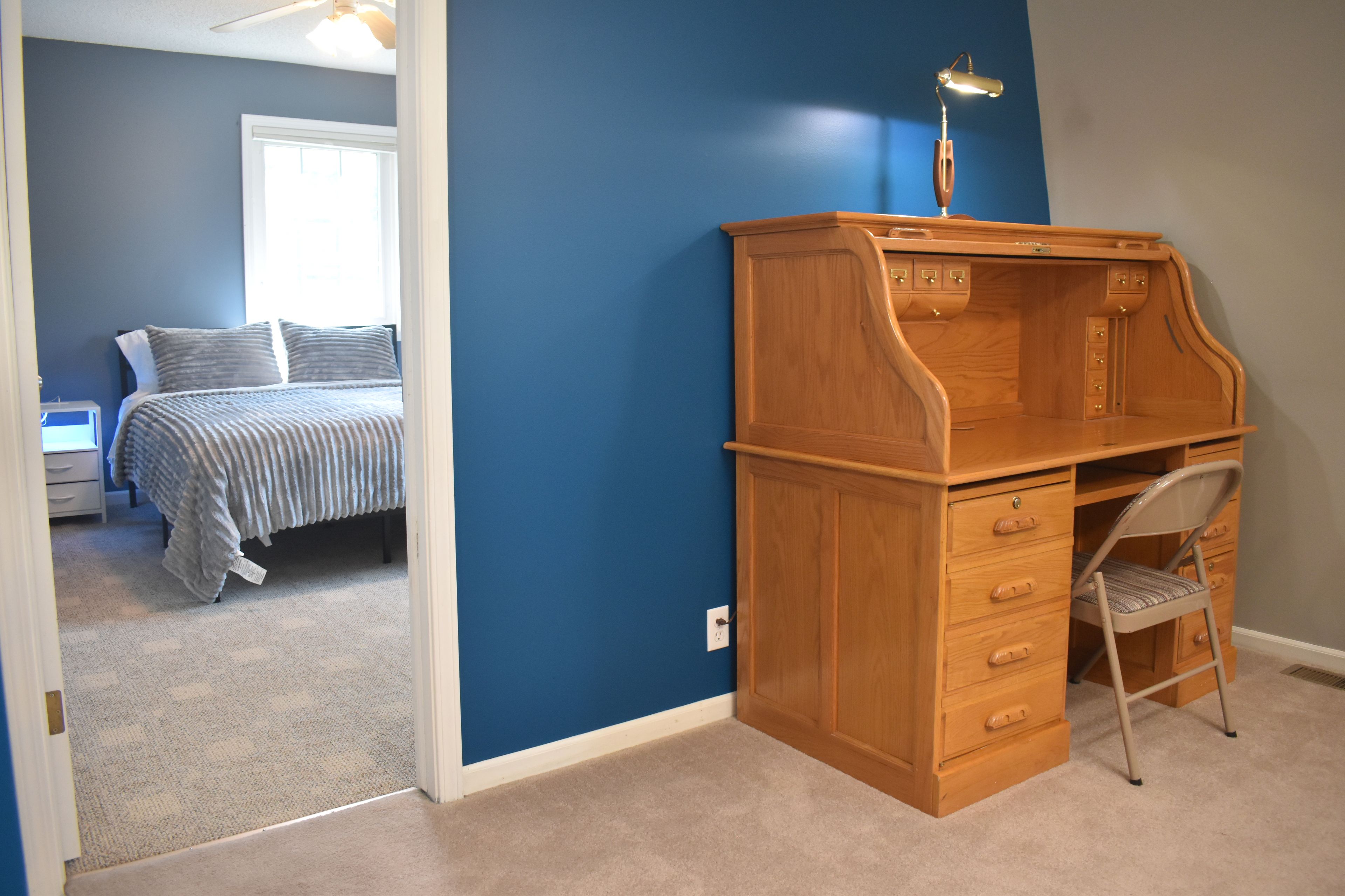 A bedroom with a bed, a desk with drawers, a chair, and a nightstand.