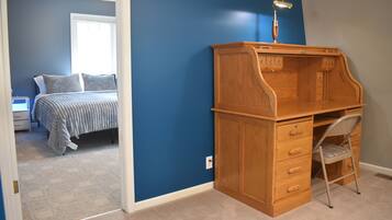 A bedroom with a bed, a desk with drawers, a chair, and a nightstand.