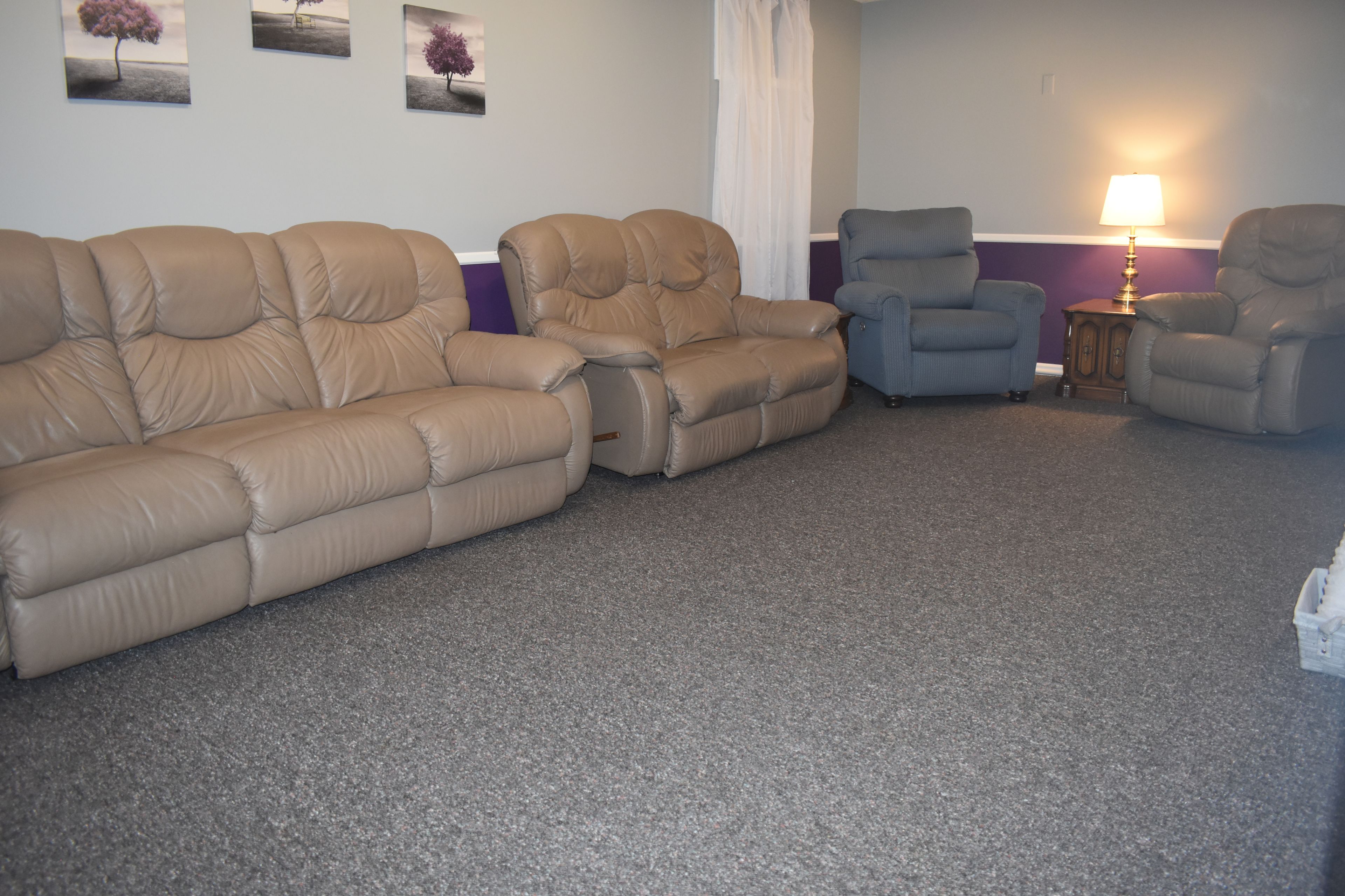 Una sala de estar con un sofá seccional color beige, un sillón azul y una mesita con una lámpara.