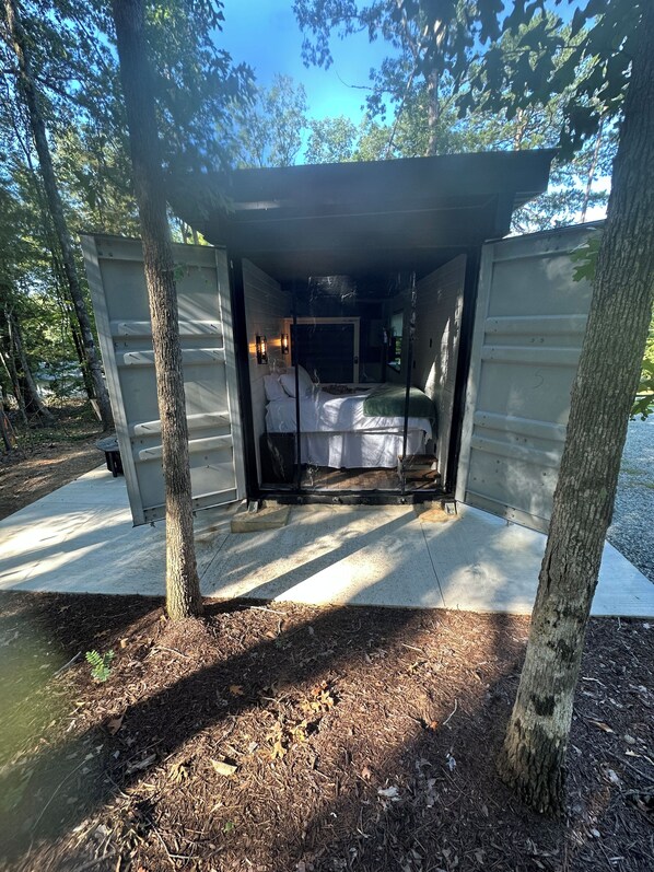 A small, enclosed cabin with a bed and a window, surrounded by trees.