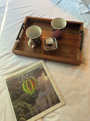 A wooden tray with two cups and a container of food on a bed.