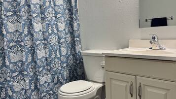 Un bagno con il water, un lavandino, uno specchio e una tenda da doccia con motivo floreale.