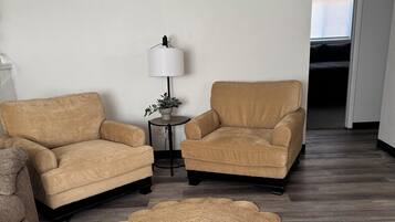 A living room with two armchairs, a small table with a lamp, and a woven rug on a wooden floor.