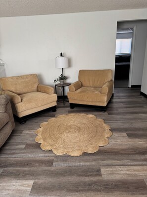 A living room with two armchairs, a small table with a lamp, and a woven rug on a wooden floor.