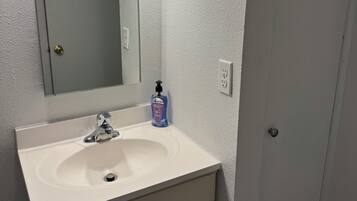 A bathroom with a white sink, a mirror, and a bottle of hand soap.