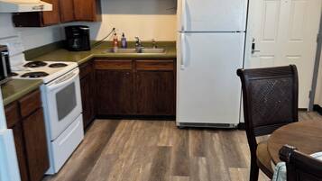 A compact kitchen with wooden cabinets, a white refrigerator, a stove, and a dining table with chairs.