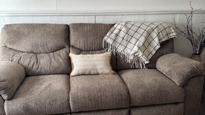 Modulaarinen sohva, jonka päällä on ruutukuviollinen huopa, sen yläpuolella on kehystetty maisemamaalaus ja lattialla on puulattia.