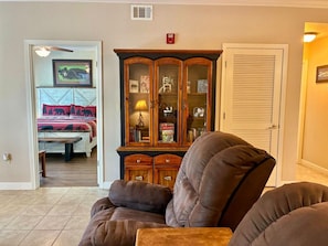 A living room with a brown armchair, a wooden cabinet with glass doors, and a bed with a red and black patterned bedspread. - Unit 5402- FREE Attraction Ticket with EACH night Stay Including Dollywood (Pigeon Forge)