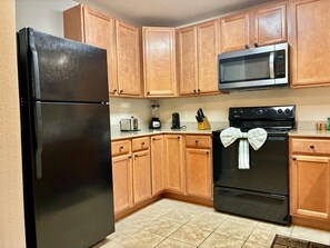 A kitchen with wooden cabinets, a black refrigerator, a microwave, a toaster, a coffee maker, and an oven with a towel tied around it. - Unit 5402- FREE Attraction Ticket with EACH night Stay Including Dollywood (Pigeon Forge)