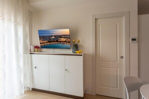 A room with a television mounted on a white cabinet, a vase with flowers, and a door. - Stella D'Oriente Apartment in Central Bari with Balcony, Wi-Fi, and Air Conditioning (Bari)