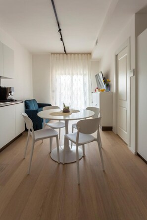 A modern kitchen with white cabinets, a coffee machine, and a dining area with a round table and white chairs. - Stella D'Oriente Apartment in Central Bari with Balcony, Wi-Fi, and Air Conditioning (Bari)