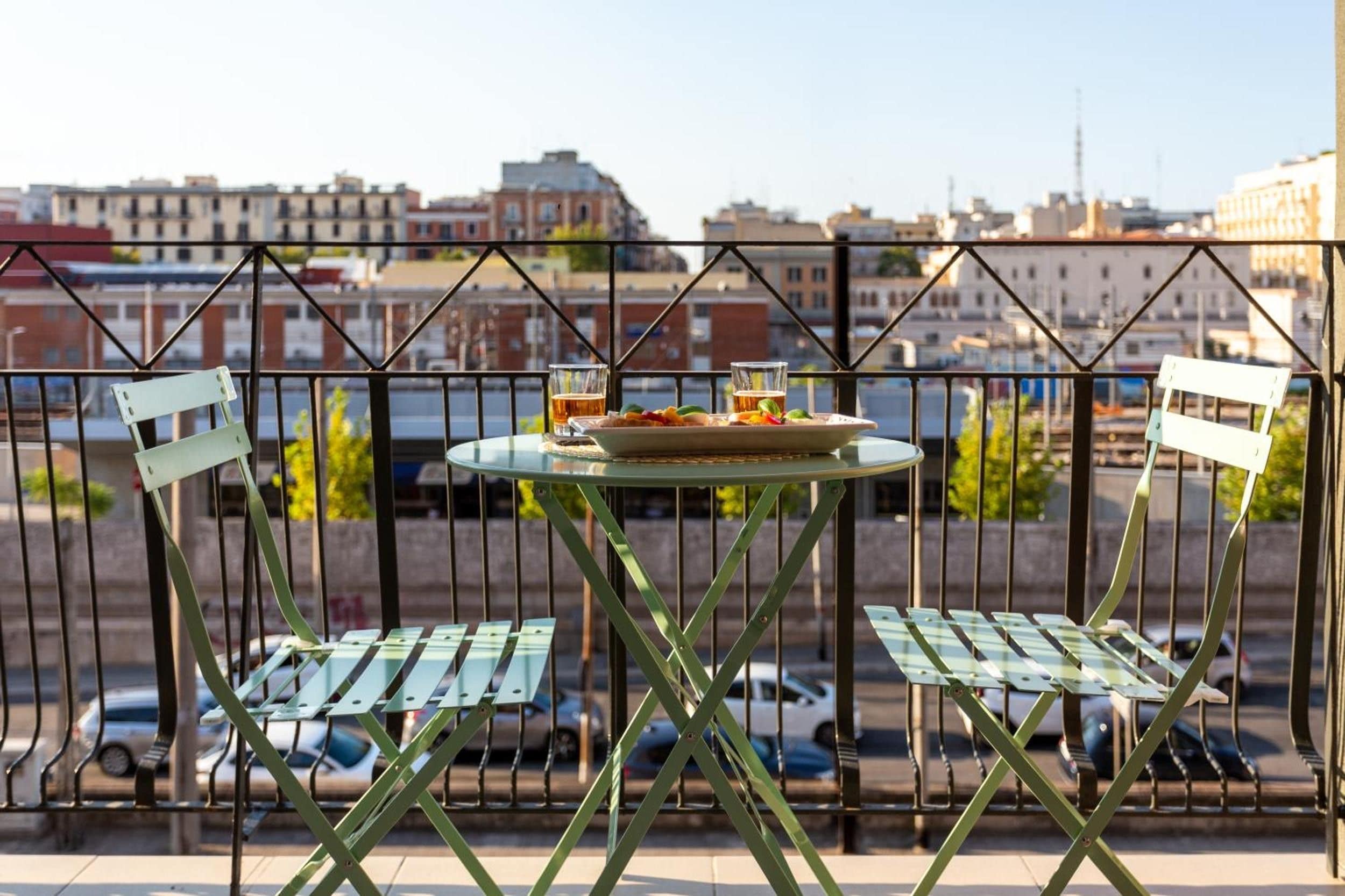 Un balcón con una mesa y dos sillas, con vistas a un paisaje urbano de edificios y coches estacionados.