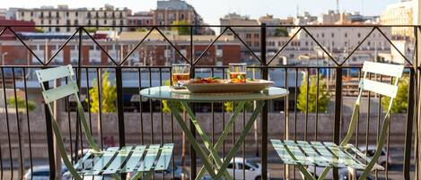 Un balcón con una mesa y dos sillas, con vistas a un paisaje urbano de edificios y coches estacionados.