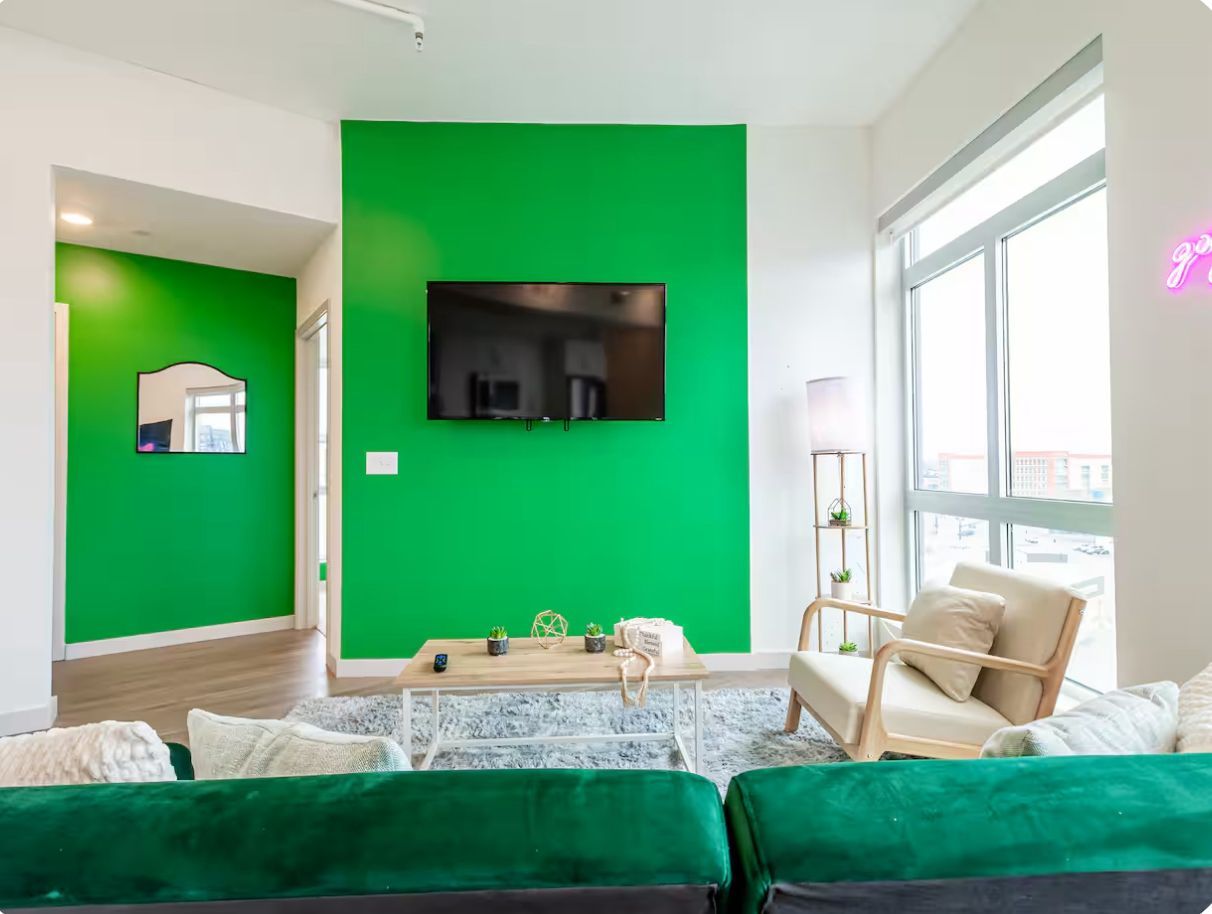A modern living room with a green accent wall, a flat-screen TV, a sofa, a coffee table, and a chair.