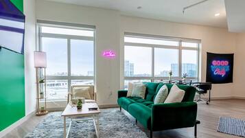 Una sala de estar moderna con un sofá verde, una mesa de centro y vistas de la ciudad a través de amplios ventanales.