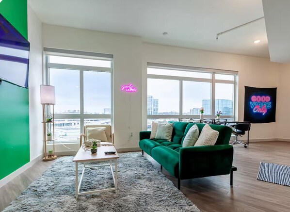 Una sala de estar moderna con un sofá verde, una mesa de centro y vistas de la ciudad a través de amplios ventanales.