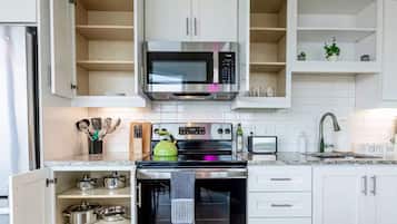Una cocina con gabinetes blancos, un microondas, una estufa y un letrero que indica barra de café.
