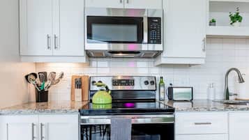 A modern kitchen with white cabinets, a stainless steel microwave, a green kettle, and a built-in oven.