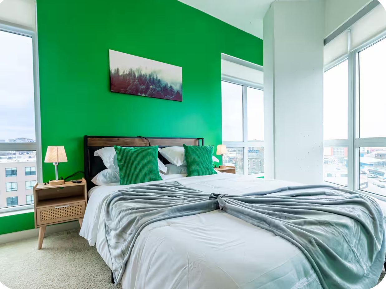A bedroom with a large bed, green walls, and a city view.
