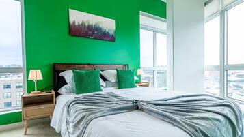 A bedroom with a large bed, green walls, and a city view.
