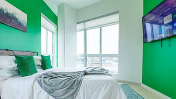 Habitación de hotel con una cama grande, una pared de acento verde, un ventanal amplio y un televisor de pantalla plana montado en la pared.