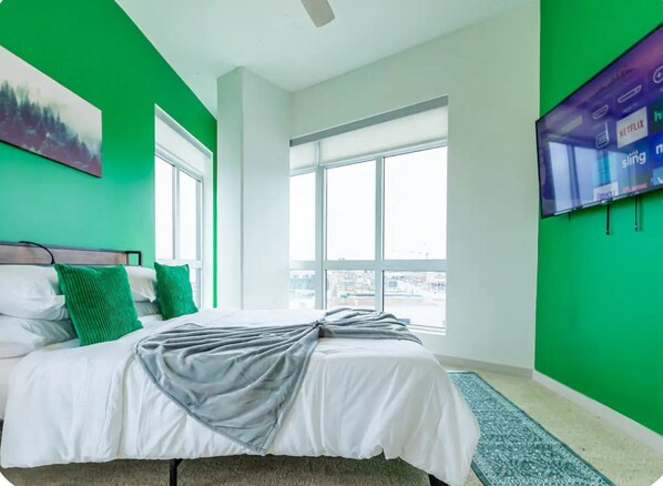 Ein Hotelzimmer mit einem großen Bett, einer grünen Akzentwand, einem großen Fenster und einem an der Wand befestigten Flachbildfernseher.