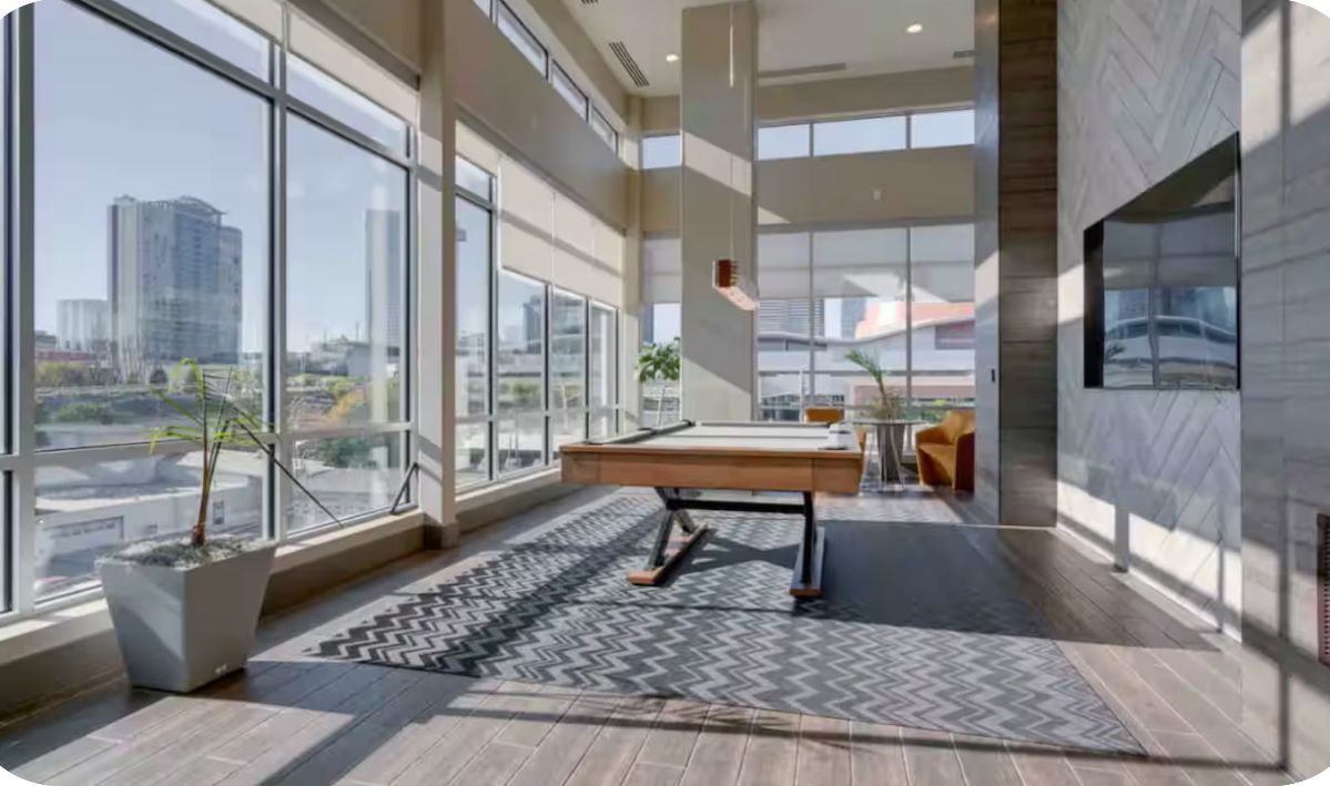 Amplio espacio interior con ventanas grandes, una mesa de billar y una planta en maceta.