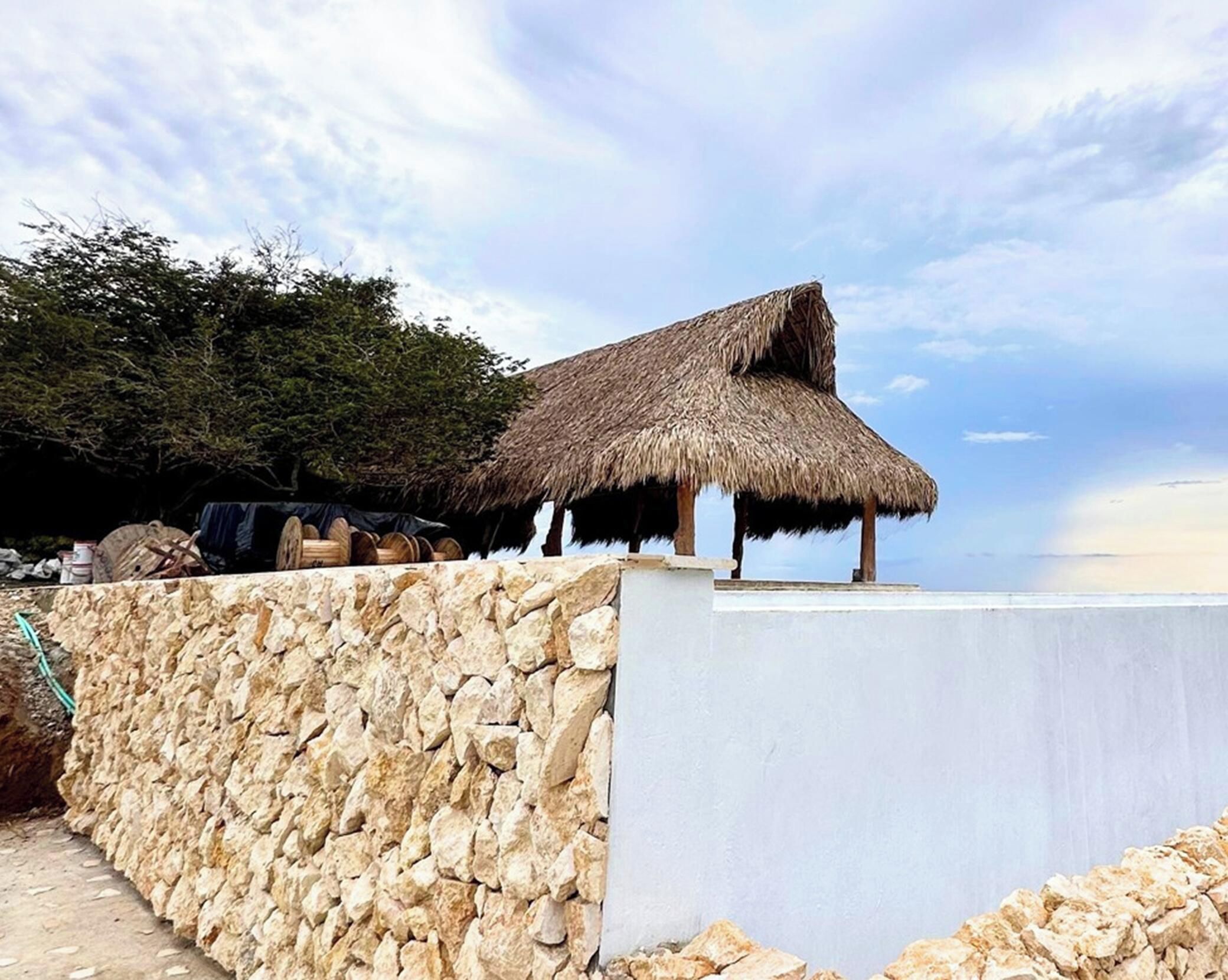 Una construcción de techo de paja con un muro de piedra al frente.