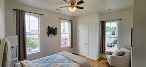 A bedroom with a bed, a ceiling fan, a window, a door, and a view of the outside.