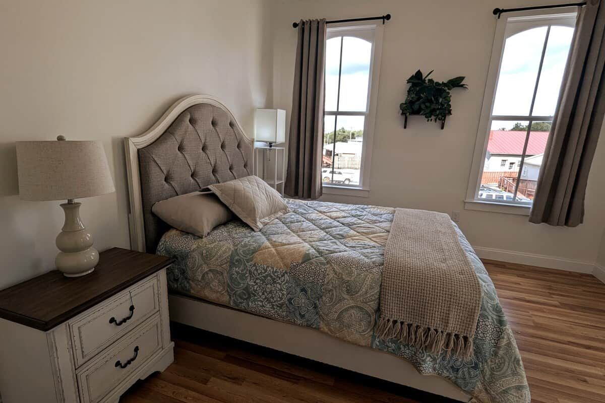 A bedroom with a bed, a nightstand, a lamp, and a window with curtains.