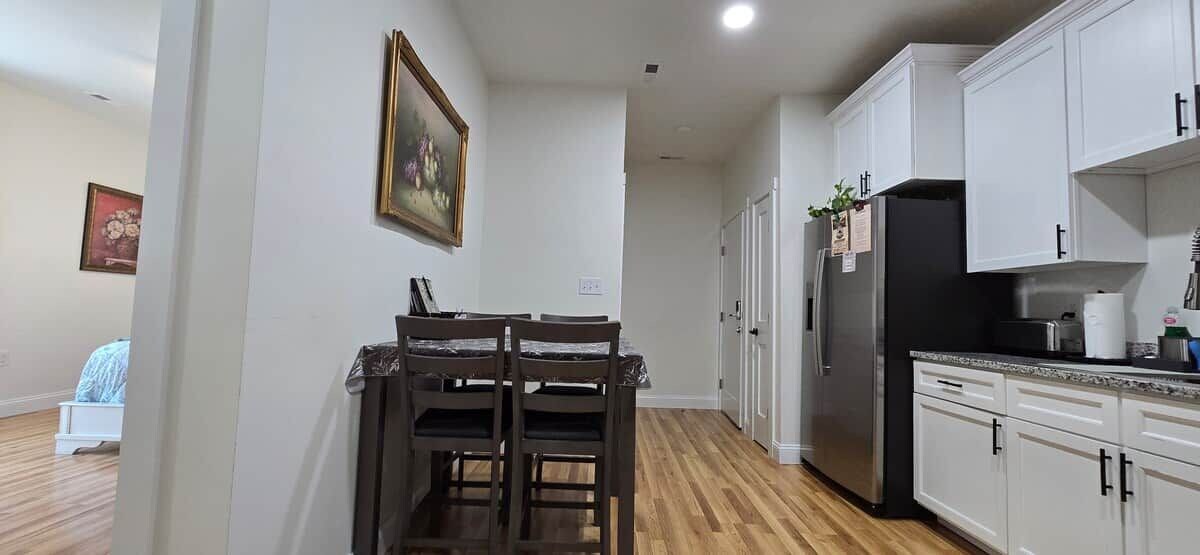 Una cocina con armarios blancos, un refrigerador negro y una mesa de comedor con sillas.